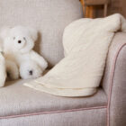 Ivory cashmere baby knit blanket draped on armchair with teddy bear nursery scene