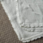 White scallop cotton baby knit blanket draped on sofa with teddy bear
