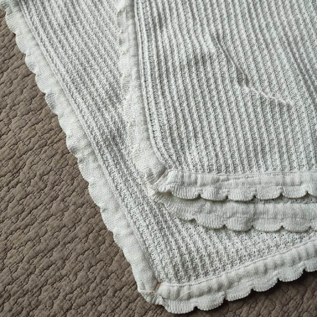 White scallop cotton baby knit blanket draped on sofa with teddy bear