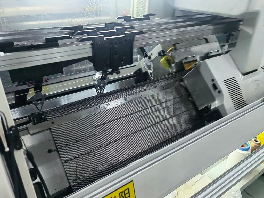 Close-up of a computerized flat knitting machine used for custom sweater production at HDL Fashion.