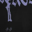 Close-up of two laddered distressed holes in the black knit below the hanging dagger motifs