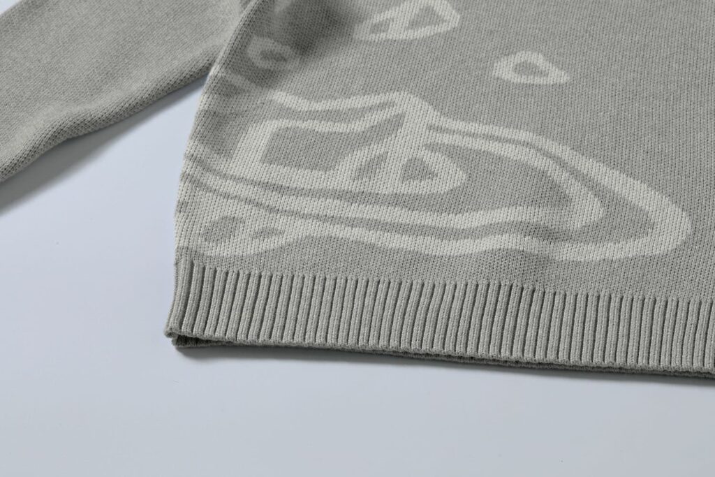 Close-up of a custom gray cotton sweater featuring a jacquard knit pattern and ribbed hem