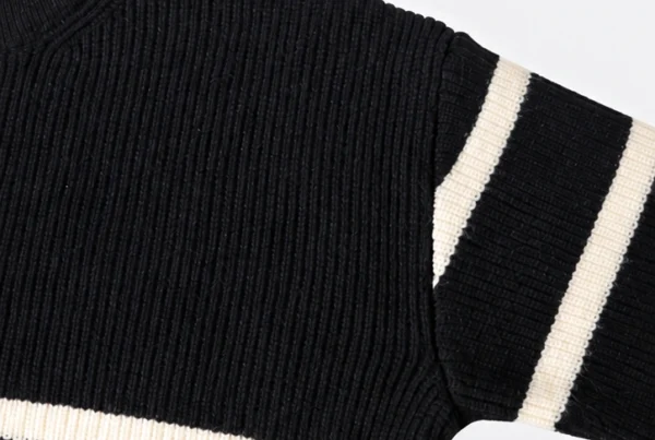 Close-up of a black knitted sweater with cream stripes, showing ribbed knit texture, shoulder seam and sleeve details