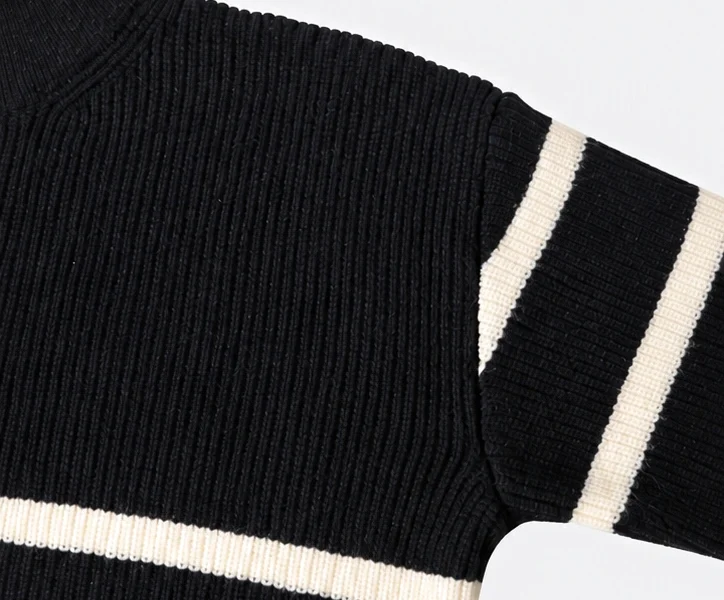 Close-up of a black knitted sweater with cream stripes, showing ribbed knit texture, shoulder seam and sleeve details