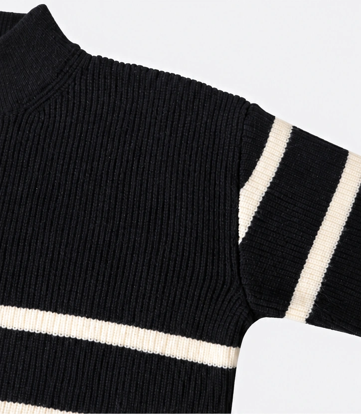 Close-up of a black knitted sweater with cream stripes, showing ribbed knit texture, shoulder seam and sleeve details
