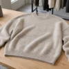 Oatmeal oversized drop-shoulder sweater laid flat on a wooden table beside yarn cones and knitted swatches.
